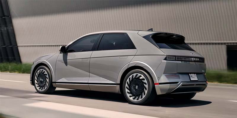 A 2024 Hyundai IONIQ 5 drives along a scenic road surrounded by trees and greenery.